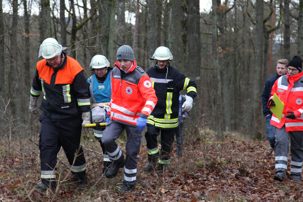 Helfer von BRK und Feuerwehr retten eine verletzte Person mit einem Spineboard aus unwegsamen Gelände.